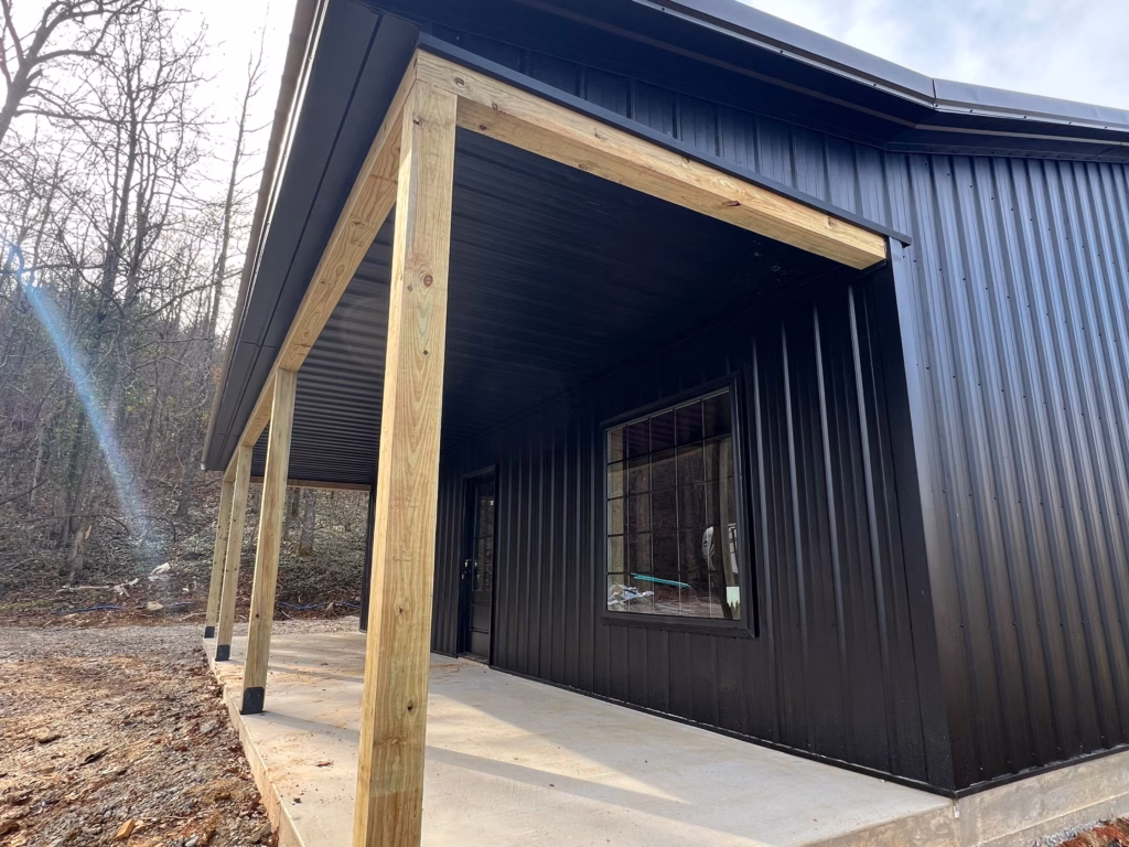 Angled front view of black barndominium with a porch right after construction was finished.