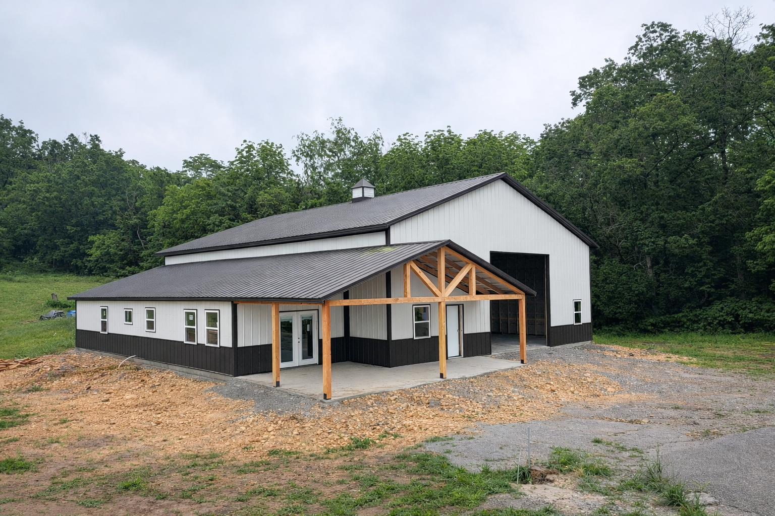 Zoomed out view of a large shop house in arkansas with white metal siding and a black metal roof.